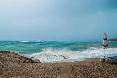 Güçlü fırtına, karanlık bulutlu gökyüzü, dalgalar ve deniz rüzgarı, dalgalar plaj şemsiyelerini sürükledi, yüzme ve sörf için tehlike