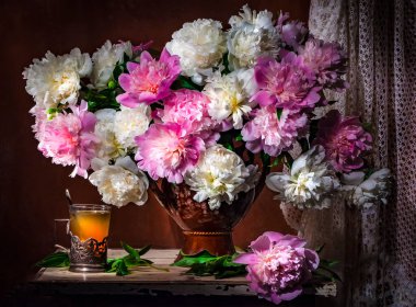 Güzel beyaz ve pembe şakayıklardan oluşan bir buket ile klasik bir hayat ve bir bardak çay, bir Rus cam tutacağında kahverengi arka planda bir ışık demeti. Sanat fotoğrafçılığı.