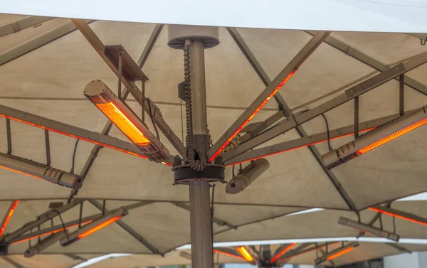 Outdoor electric heating infrared lamps under umbrella in street cafe in cold season (winter, autumn or spring)