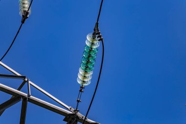 Şeffaf bir turkuaz yüksek voltaj yalıtıcısını kapat ya da mavi gökyüzü arka planındaki elektrik kulesinde güneş ışığında izolatör kullan. Elektrik güç iletim hattı