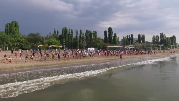 Vista aérea de varios cientos de personas hacen ejercicios deportivos en la orilla del mar en tiempo soleado — Vídeo de stock