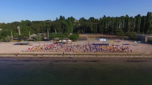 Luchtfoto van een groep van driehonderd mensen die 's ochtends oefeningen doen op de Zwarte Zee. Sportactiviteiten op het strand. — Stockvideo