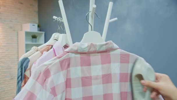 In Großaufnahme nimmt das junge Mädchen im Showroom einen rosa gestreiften Pyjama vom Kleiderbügel und beginnt, ihn mit einem Dampfbügeleisen zu dampfen. 4K FOOTAGE — Stockvideo