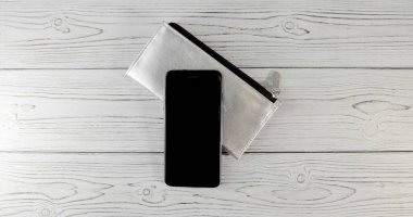 Siyah tokalı gümüş bir cüzdan ve ahşap arka planda iki kamerası olan pahalı bir siyah akıllı telefon. Üst Manzara. Düz Yatay