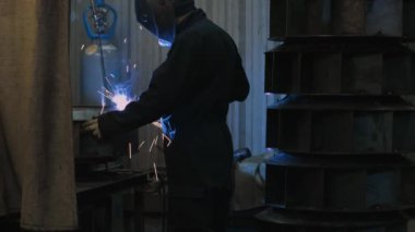 Koruyucu maskeli yakın plan demirci metal ve demirle kaynak makinesi, parlak kıvılcımlar ve parıltılar kullanarak çalışır. 4K Görüntü