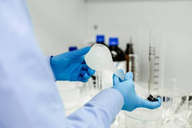 Bilim adamının elinde deney tüpleri, bilim ve tıbbi araştırma ve geliştirme konseptine kimyasal sıvı damlatan bir matara. Arka planda pipet, matara ve şişe var.