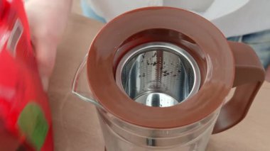 Sabahları siyah çay demleyen bir kadının yakın çekimi. Çaydanlığa siyah çay doldurur..