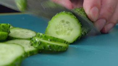 Sebzeler pişiyor. Salatalık kesme işlemi. Bir adam elinde bir sebze tutuyor. Yakın çekim görüntüsü. Tam HD