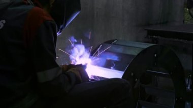 Koruyucu maskeli bir demirci kaynak makinesi ve parlak kıvılcımlar kullanarak metalle çalışır. 4K Görüntü