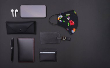 Siyah arka planda kadın yönetici seyahat aksesuarları: antibakteriyel jel, yüz maskesi, cep telefonu, bluetooth hardhone, kalem, kart tutucu, pasaport ve güneş gözlüğü kutusu. Üst görünüm noktası.