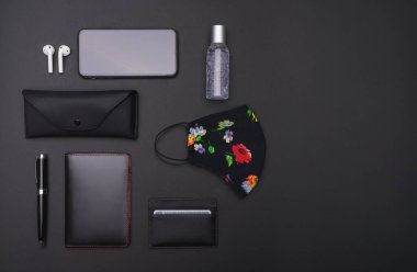 Siyah arka planda kadın yönetici seyahat aksesuarları: antibakteriyel jel, yüz maskesi, cep telefonu, bluetooth kulaklık, kalem, kart tutucu, pasaport ve güneş gözlüğü kutusu. Üst görünüm noktası.