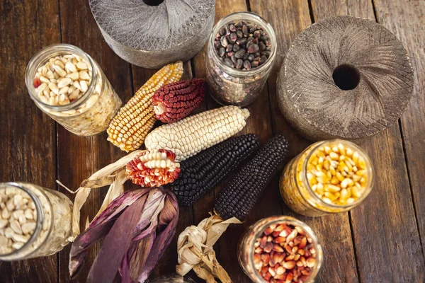 Sweet corn, white corn, red corn, blue corn and grinding stones on wooden table, flat lay.