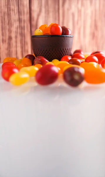 Various colorful cherry tomatoes on white and wooden background. Creative design, beautiful lighting.