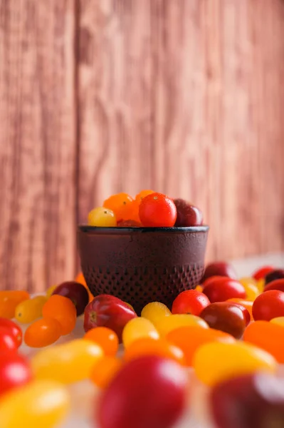 Various colorful cherry tomatoes on white and wooden background. Creative design, beautiful lighting.