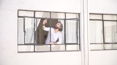 Pencerede telefonu sosyal mesafede olan bir adam. Penceredeki adamın video çağrısı var.