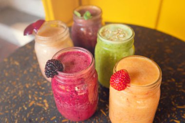 Ahşap masa üzerinde meyve süslemeli renkli meyve suları ve sarı arka plan. Sağlıklı içki konsepti. Sağlıklı içecekler