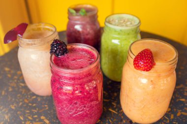 Ahşap masa üzerinde meyve süslemeli renkli meyve suları ve sarı arka plan. Sağlıklı içki konsepti. Sağlıklı içecekler