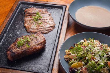 Farklı tabaklar, biftek, salata ve çorba. Tahta masadaki farklı yiyecekler. Üç menü