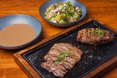 Farklı tabaklar, biftek, salata ve çorba. Tahta masadaki farklı yiyecekler. Üç menü