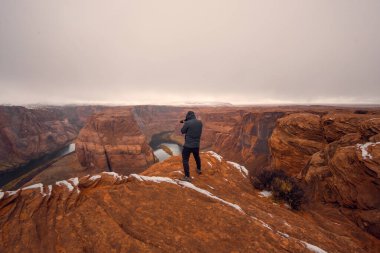 Bulutlu bir havada Colorado Nehri 'nde at nalı üzerinde fotoğraf çeken bir adam. At nalı kıvrımının panoramik görüntüsü