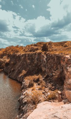 Mavi gökyüzünün altında nehir ve tepelerle dolu yüksek bir taş ocağı.