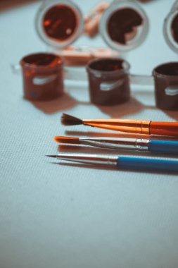 Resim yapmak için üç fırça boyaların yanında beyaz bir arkaplanda uzanır..