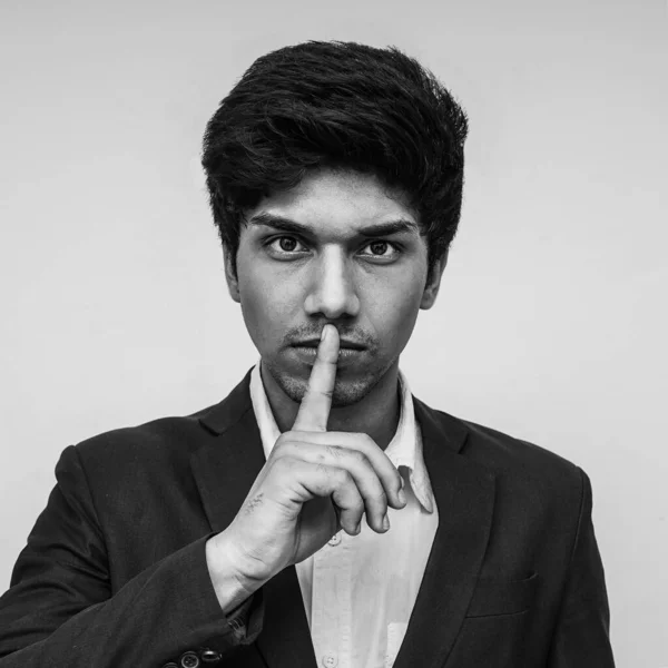 close up studio portrait of young boy with finger on his lips in silence and shut up hand gesture warning or threatening not to speak in political censorship and coerced freedom of speech