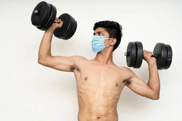 Fitness man with mask for epidemic protection working exercise for arm,biceps, and shoulders with dumbbells.Training in epidemic time