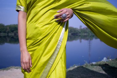Yeşil geleneksel sari giyen güzel Hintli genç model nehir manzarasının önünde duruyor..