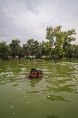 Delhi, Yeni Delhi, Hindistan - 26 Mayıs 2020: Sıcak yaz gününde Hindistan kapısının yakınındaki bir gölde oynayan mutlu Asyalı çocuklar. Neşeli ve tasasız çocuklar..