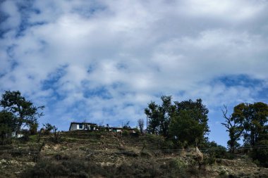 Tepesinde bulutlar olan bir dağın tepesinde bir kulübe..