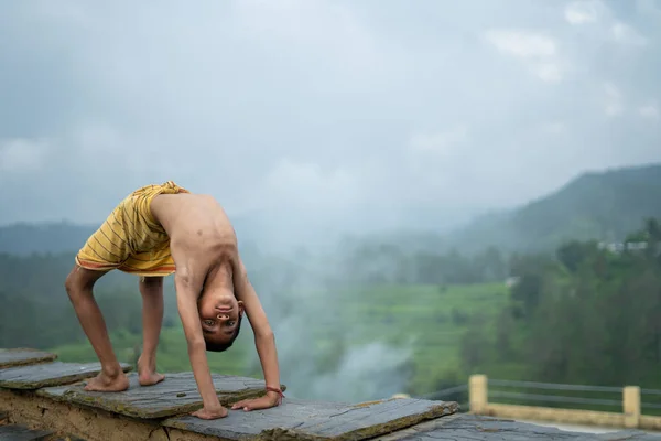 Genç Hintli şirin bir çocuk dağlarda yoga yapıyor, dhoti giyiyor.