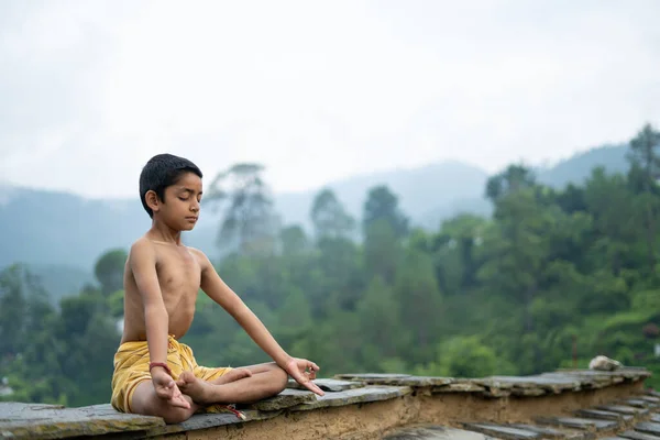 Genç Hintli şirin bir çocuk dağlarda yoga yapıyor, dhoti giyiyor.