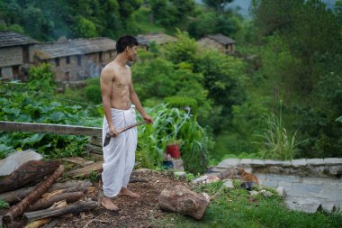 Beyaz dhoti giyen genç bir çocuk baltayla odun kesiyor..