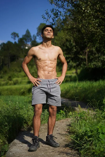 Genç, yakışıklı, yırtık pırtık bir çocuk yolda üstsüz duruyor. Fitness ve sağlık.