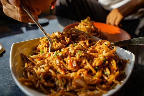 Chef picking up the Schezwan Noodles or Chiken Hakka Noodles or chow mein is a popular Indo-Chinese recipes, served in a bowl or plate with the help of spoon.
