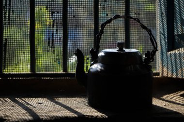 Eski ve antika siyah çaydanlık, güneş ışınlarının içeri girdiği yerin penceresinin yanında duruyordu..