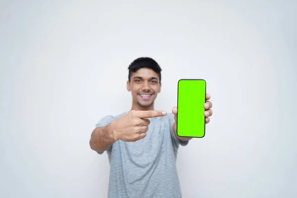 Genç Hintli yakışıklı çocuk yeşil ekranla cep telefonunu işaret ediyor. Teknoloji ve internet..