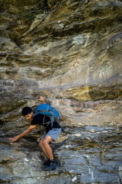 Sırt çantasıyla kayalara tırmanan genç bir çocuk..