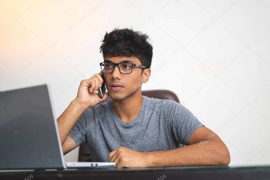 Indian boy talking over phone while working in office.