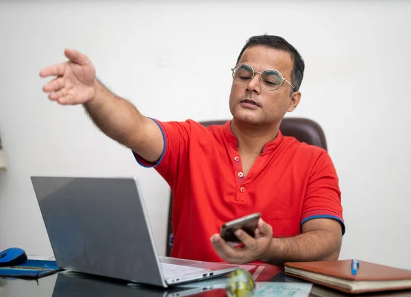 technology, remote job and lifestyle concept - happy indian man in glasses with laptop computer working at office.