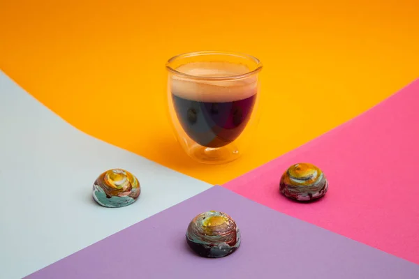 Tam siyah kremalı espresso bardağı ve renkli yuvarlak süt çikolataları. Renkli arka planda izole edilmiş fotokopi alanı olan gezegenlere benziyorlar.