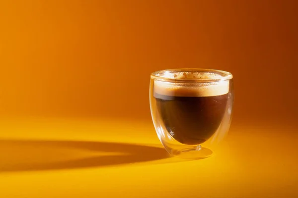 Sarı arka planda izole edilmiş cam bir kahve fincanında taze demlenmiş kremalı espresso.