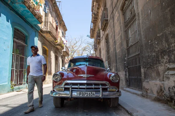 Havana / Küba - 04.15.2015: Havana sokaklarına park edilmiş klasik (antika), kırmızı, parlak bir arabanın yakınından geçen yerel bir adam, Küba