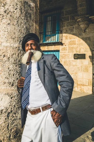 Havana / Küba - 04.16.2015: Uzun beyaz sakallı, siyah askeri bereli, büyük bir puro içen Afro Kübalı yaşlı adam
