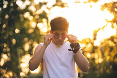 Gün batımında bir çocuk gözlüğünü takıyor ya da çıkarıyor ve kameraya bakıyor.