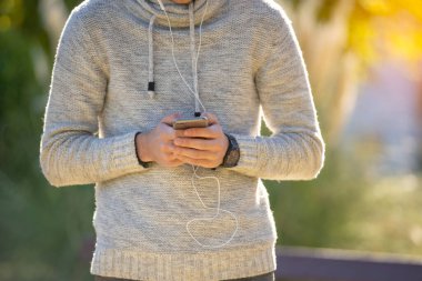 Parktaki gri kazaklı, cep telefonlu genç adam.