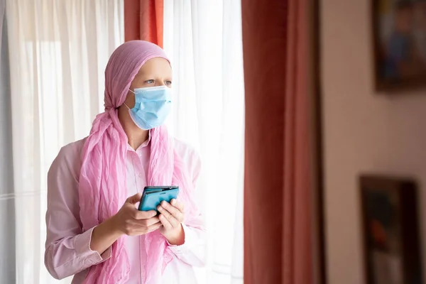 Kanserli kadın, pembe başörtüsü ve cep telefonunda yazı yazan maske.