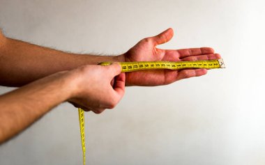Sol elini parmaklarından bileğine kadar sarı bir mezura ile ölçen kişi. Beyaz arka plan. Zeytin tonu. 