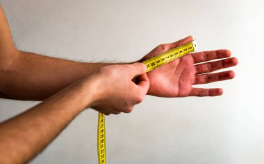 Sol elinin baş parmağını sarı bir mezura ile ölçen kişi. Beyaz arka plan. Zeytin tonu. 